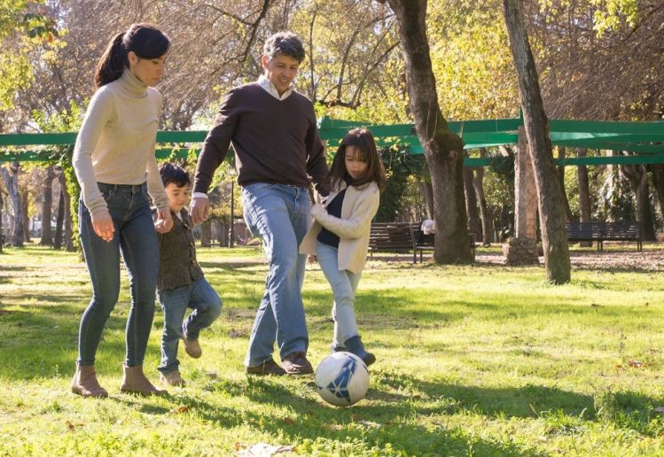 A family plays soccer together in a sunny park, enjoying quality time outdoors.
