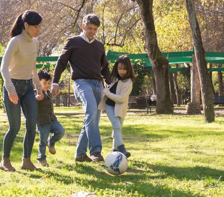 A family plays soccer together in a sunny park, enjoying quality time outdoors.