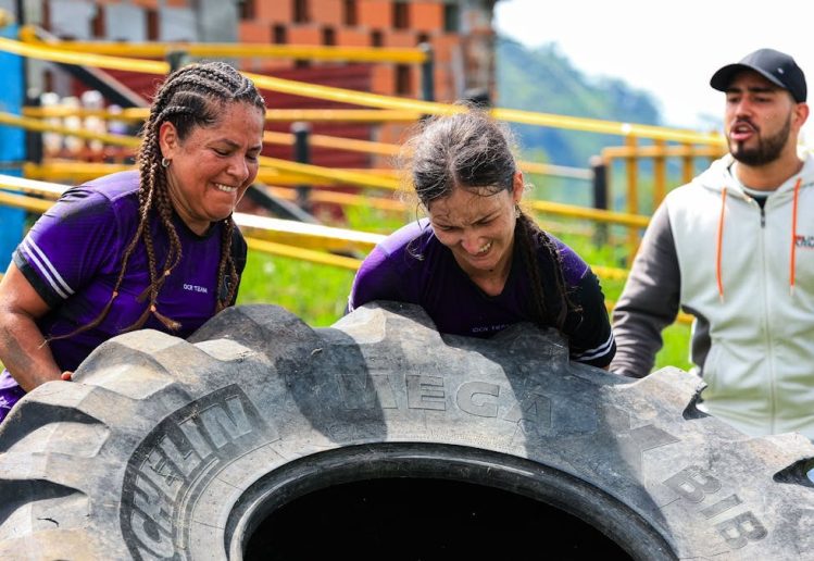 Two women and a man engage in an outdoor fitness session flipping a large tire.