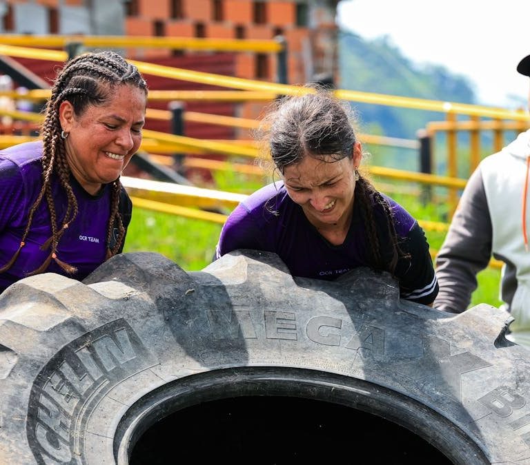 Two women and a man engage in an outdoor fitness session flipping a large tire.